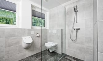 A modern bathroom with a shower and a toilet.  
Large windows provide plenty of natural light and a view of the greenery.