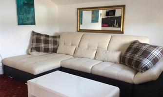 A modern living room with a beige sofa and checkered cushions. A white table and a mirror complete the cozy atmosphere.