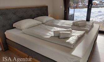A modern bedroom with a double bed and fresh towels.  
Natural light pours in through large windows, and the view of the snowy landscape is visible.