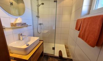 A modern bathroom with a glass shower and an elegant sink. The walls are clad with white tiles, and there are orange towels.