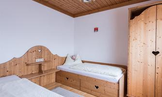 A cozy bedroom with light wooden furniture. There are two beds, a wardrobe, and a warm atmosphere.
