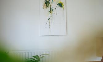 A painting of a sunflower hangs on the wall. In the foreground, some green plants are visible.