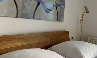 A cozy bedroom with a wooden headboard and two white pillows. A picture of blue flowers hangs on the wall.