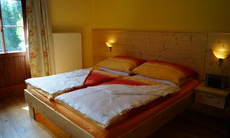A cozy bedroom with a double bed and colorful bedspreads. The room has warm colors and a window overlooking nature.