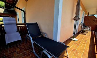 A balcony with two loungers and a sun umbrella. The walls are painted in soft colors and the floor is tiled.