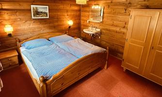 A cozy bedroom with a double bed and wooden walls. There is a small bedside lamp and a wardrobe.