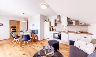 A modern living room with an open kitchen and a dining table. The decor is bright and inviting, with wooden flooring and elegant furniture.