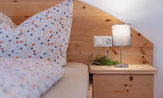 A cozy bedroom with a bed and colorful cushions. A small lamp and some greenery are on the nightstand.