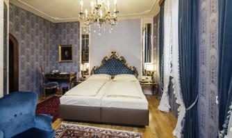 An elegant bedroom with a luxurious double bed and a stylish chandelier. The walls are decorated with blue wallpaper, and the room has a cozy atmosphere.