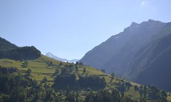 A picturesque mountain landscape with green meadows and high mountains. The sky is clear and the sun is shining on the hilly landscape.