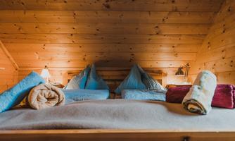 A cozy bedroom in the attic with wooden ceilings. On the bed are pillows and towels in various colors.