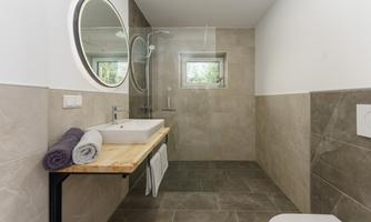 A modern bathroom with a large round mirror surface. There is a sink on a wooden shelf and fresh towels.