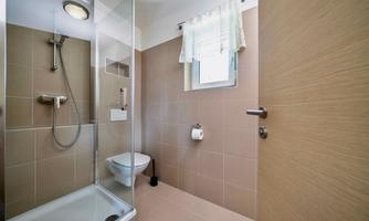 A modern bathroom with a shower and a toilet. Bright tiles and a window create a cheerful atmosphere.