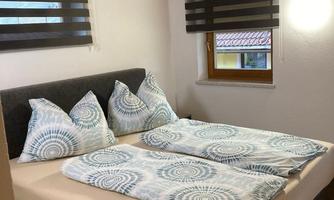 A cozy bedroom with a large double bed and decorative pillows. Bright walls and a wooden ceiling create a pleasant atmosphere.