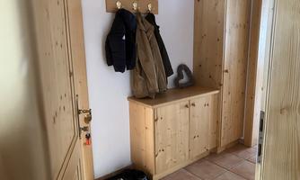 A bright hallway with wooden shelves and a shoe cabinet. Some jackets and a heart decoration piece hang on the wall.