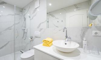 A modern bathroom with marbleized walls and an elegant shower. On the sink lie two yellow towels.