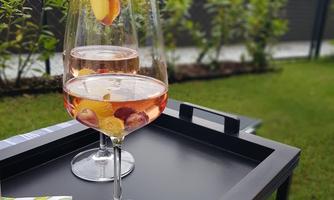 Two glasses with fruity drinks on a black tray, decorated with fruit slices. In the background, a green landscape can be seen.