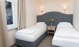 A bright room with two single beds and soft colors. On the nightstand is a small vase with fresh tulips.