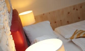 A cozy bedroom with a red headboard and white bedding. Two lamps provide soft light.