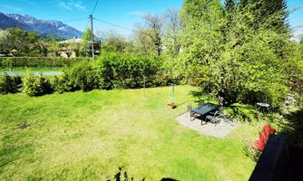 A green garden with a lawn and a table set. In the background, trees and the mountains can be seen.