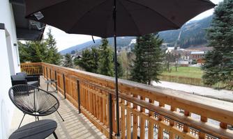 A balcony with two chairs and a sunshade. In the background, trees and mountains can be seen.