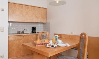 A bright kitchen with a wooden table and chairs. On the table is a breakfast with rolls, juice, and coffee.