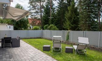 A well-maintained garden with grass and a paved path. There are lounge chairs and a terrace with furniture.