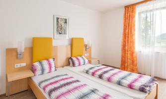 A modern bedroom with two single beds and colorful bedspreads. Large windows provide plenty of natural light and a fresh atmosphere.
