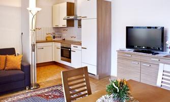 A modern kitchen unit with a cozy living room. The room is bright and pleasantly furnished, with a table and a television.