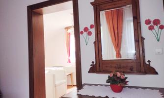 A cozy room with a wooden table and a mirror. Through the door, a bright living area with white furniture is visible.