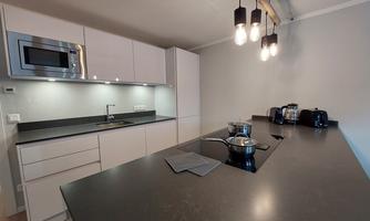 A modern kitchen with simple, white cabinets and a dark countertop. It is well-lit and contains several kitchen appliances.