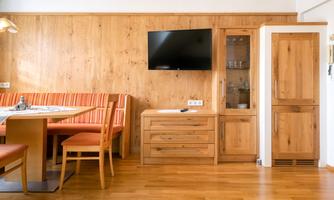 A bright room with wooden walls and a TV on the wall. The dining area is furnished with a table and chairs in warm colors.