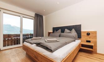 A modern bedroom with a large double bed and elegant wooden paneling. Large windows offer a view of the mountains.