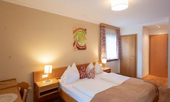 A cozy bedroom with a double bed and modern wooden furniture. The warm colors and the windows create an inviting atmosphere.