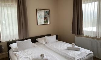 A cozy room with two single beds and fresh towels. Large windows provide plenty of daylight.