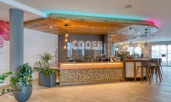 A modern reception area with a stylish counter and comfortable seating. The design is bright and inviting, featuring plants and warm wood accents.
