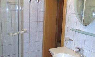 A simple bathroom with a shower, a sink, and a mirror. The walls are tiled and there is a wooden frame on the door.