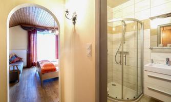 A bathroom with a shower and modern sink. In the background, there is a cozy bedroom with a window and a bed.