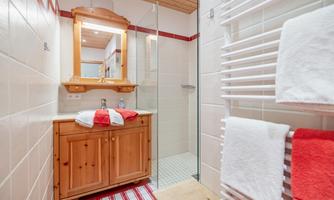 A modern bathroom with a shower and a wooden washbasin. Radiators hang beside the towels and a large mirror is present.
