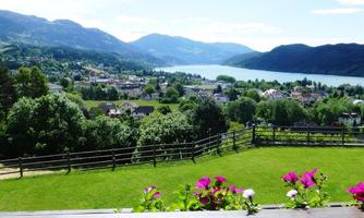 A picturesque view of a village by the lake, surrounded by green hills and mountains. Colorful flower frames in the foreground give the image a vibrant accent.