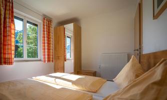 A bright bedroom with two beds and large windows. The curtains are checked, and the furnishings are modern and friendly.