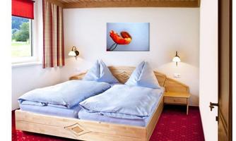 A cozy bedroom with a double bed and blue bedspreads. A picture of a flower hangs on the wall, while light shines from two wall sconces.