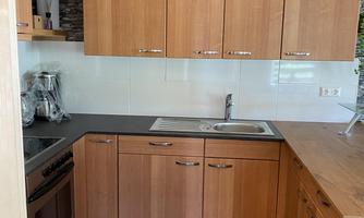 A modern kitchen with wooden cabinets and a light countertop. The equipment includes a stove, a sink, and appliances on the countertop.