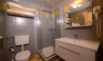 A modern bathroom with a shower, a toilet, and a sink. The walls are designed with gray tiles and yellow accents.