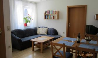 A cozy living room with a blue sofa and a wooden table. In the background, there are bookshelves and a television.