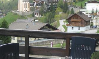 A beautiful view from a balcony of a picturesque village in the mountains. Tables are set with dishes, while in the background a church and green hills are visible.