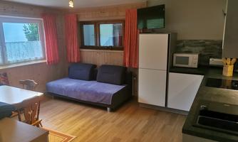 A cozy living room with a sofa, a dining table, and a modern kitchen. There are large windows with curtains and a calm atmosphere.
