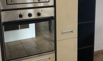 A modern kitchen with a stainless steel oven and microwave. The cabinet has a light color and open shelves on the right side.