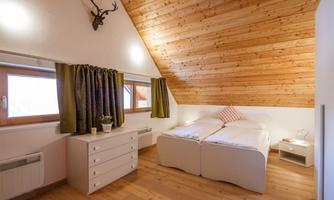 A cozy bedroom with a wooden ceiling and two single beds. The walls are light, and there is a simple chest of drawers as well as curtains in dark green.