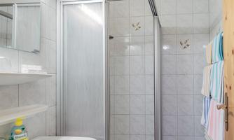 A small bathroom with a shower cabin and a sink. The walls are tiled, and there are colorful towels in the background.